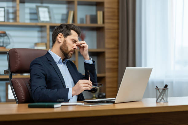 maschio barbuto sovraccarico di lavoro che tiene gli occhiali da vista e strofina gli occhi asciutti e irritati dopo aver guardato troppo a lungo lo schermo del laptop. uomo esausto che ha una cattiva vista e fa una pausa per la distrazione visiva dal lavo - human eye tired rubbing businessman foto e immagini stock