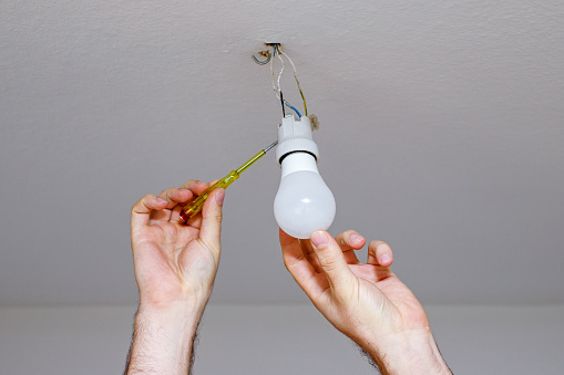 hands of male electrician fixing chandelier with use of professional tools