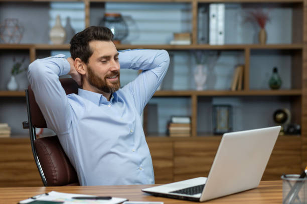 istock Relaxed brunette man leaning back and holding hands behind head in personal workspace with pc. Calm head of company taking break during busy day and enjoying daydreaming in comfortable chair 2027821652