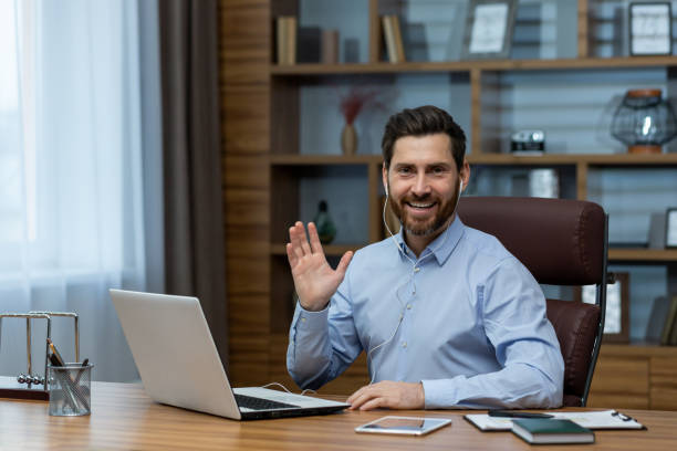 istock Friendly businessman waving in a video call while working in a home office setup 2027822193