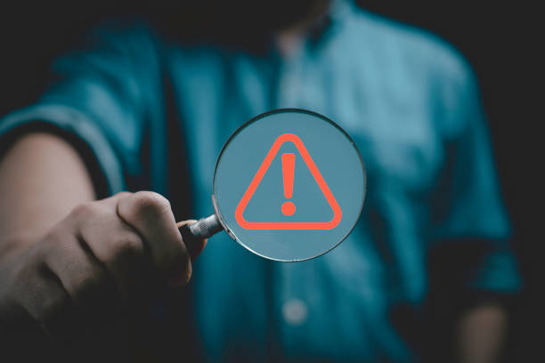 istock Businessman holding magnifier glass with red triangle caution warning sign for notification error and maintenance concept. 2027833935