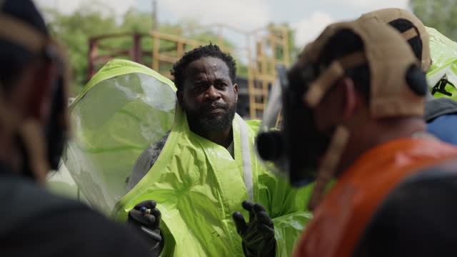 Group of confident safety experts in hazmat suit gathers for an intense session of Planning, Discussion, and Explaining as they meticulously strategize the cleanup of a chemical spill at the facility.