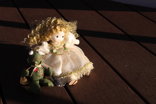 The photo is of a doll sitting on a wooden floor. The doll is wearing a dress with a frog attached.