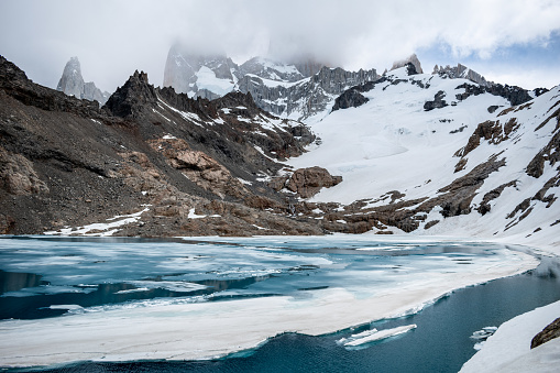 Beautiful image of Laguna de los Tres at the foot of Mount Fitz Roy. Beautiful postcard of Mount Fitz Roy. Cerro fitz Roy covered by clouds. Frozen Laguna de los Tres at the foot of Mount Fitz Roy