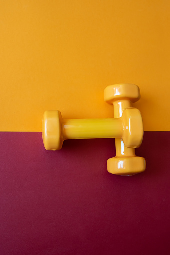 Two orange dumbbells on orange and red background with copy space. A tool for training, sport and activity in summer time.