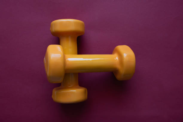 Two orange dumbbells on red background with copy space. A tool for training, sport and activity in summer time.