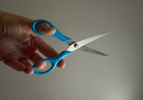 hand taking scissors for trimming, blue-colored scissors of two silver blades with edge