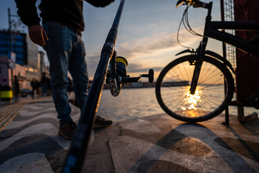 fishing rod is in man hand focus on foreground sunset and cycle are background horizontal still