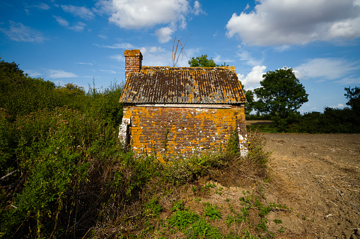 A dilapidated, brick Lookers Hut sits on the edge of a ploughed field in a sunny day.