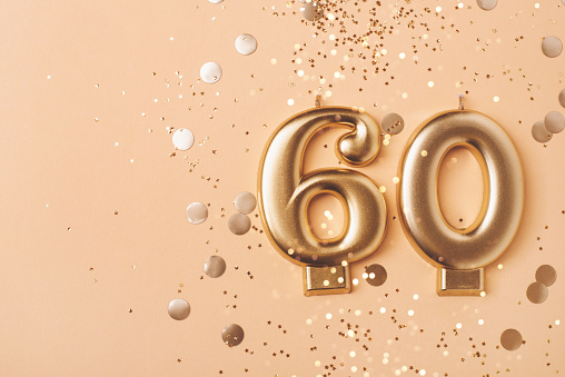 60 years celebration. Greeting banner. Gold candles in the form of number sixty on peach background with confetti.