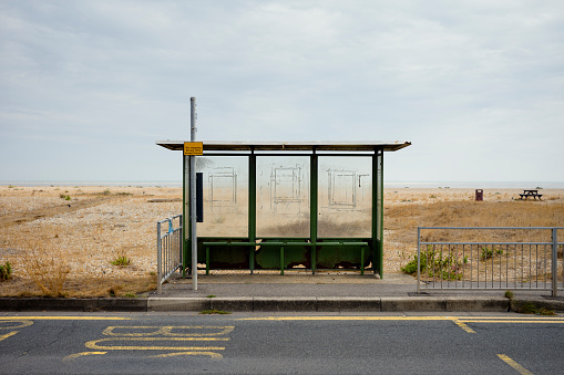 An empty and lonely looking bus stop with a shingle beach behind it and a sea horizon on a bright but grey day,
