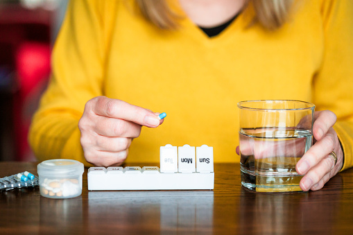 A senior woman organising her medication into a pill box at home.