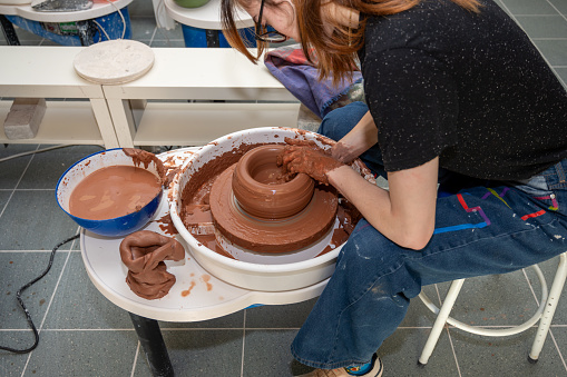 Side view of young woman's hands molding clay on pottery wheel