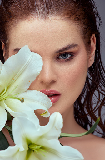 Portrait of a beautiful woman with clean skin, holding a bouquet of Casablanca flowers on her face.