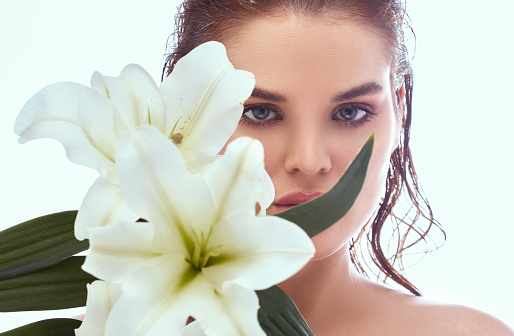 Portrait of a beautiful woman with clean skin, holding a bouquet of Casablanca flowers on her face.