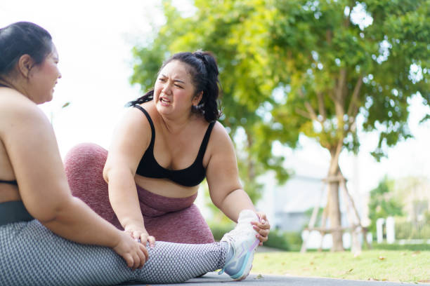 Woman got an accident during exercise. Close up shot of Asian oversized fat woman having an accident at her leg and her friend comes to help or support her. Oversized woman got an accident and her friend trying to do a first aid. obese joint pain stock pictures, royalty-free photos & images