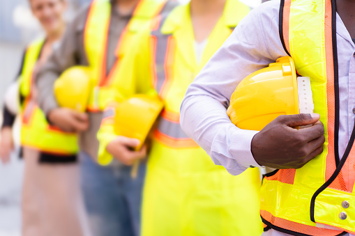 Close up shot of engineer or foreman team holding a protective safety helmet beside their body. A shipyard - container yard workers and logistic engineers holding a yellow safety hardhat or helmet.