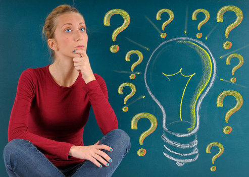 Young woman with question mark and light bulb on blackboard