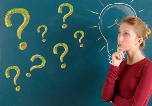 Young woman with question mark and light bulb on blackboard