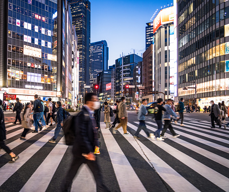 Motion blur on a side view of a wide, busy crossing in Shibuya, Tokyo at dusk.
