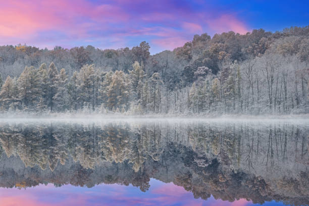 Foggy autumn landscape of the shoreline of Deep Lake flocked with snow and with mirrored reflections in calm water, Yankee Springs State Park, Michigan, USA