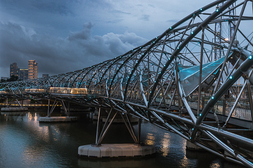 Helix Bridge in Singapore City over the Singapore River under dark dramatic thunderstorm cloudscape in after sunset twilight. Double Helix Bridge, Marina Bay, Singapore, Southeast Asia.