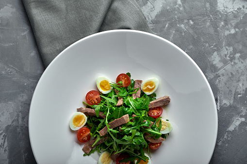 Tasty italian salad of beef tongue with eggs, arugula, tomato, spices and sauce.