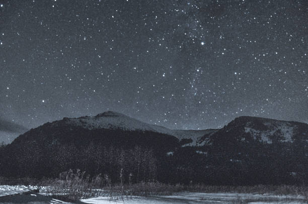 A mountainous landscape blanketed in pristine snow, illuminated by a starry night sky creating a tranquil and atmospheric atmosphere. Russia, Siberia, Altai mountains.