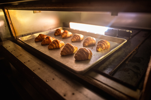 Croissants baking in the oven alongside a baking sheet filled with buns in a commercial kitchen at a cooking school.