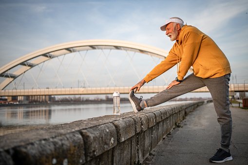 A vigorous older gray-haired man defies his years as he exercises outdoors. With a smile on his face, he performs various exercises that testify to his strength and agility. Sunlight offers additional warmth to the environment