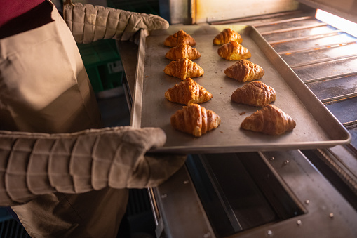 A close-up of a baking trainee holding a baking sheet filled with freshly baked buns from the oven in a commercial kitchen at a cooking school.