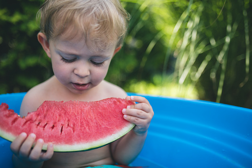 Cute little toddler boy taking a bath in garden and eat watermelon