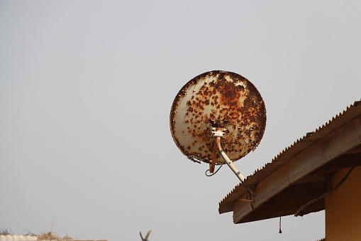 A rusted digital satellite receiver hanging from the roof of a dejected building