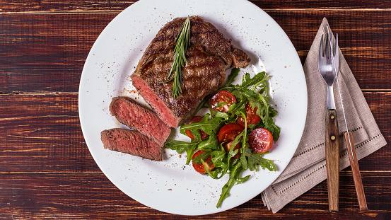 Ribeye steak with arugula and tomatoes on  dark wooden background.