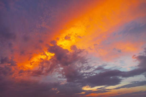 The sky background of nature's forces as rare orange clouds dominate the sky, juxtaposed against a menacing black cloud cover during sunset. This wild-looking weather system is illuminated with a golden hue, creating an abstract background texture that embodies the raw power and beauty of an untamed storm. Experience the breathtaking intensity of nature's spectacle in this captivating scene