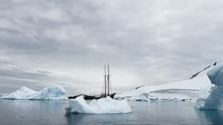 retro style sailing schooner during the huge iceberg in the Antarctic peninsula at the South Pole, waves of the southern ocean in cloudy weather