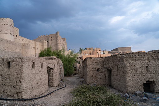 Ruined mud houses of old village around the historic Bahla Fort located at Djebel Akhdar highlands in the Sultanate of Oman against blue sky.