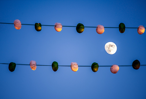 Waxing gibbous moon between two lines of paper lanterns during a festival, Seville, Spain.
