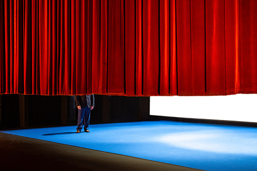 An actor half covered by the curtain at the end of a play at a playhouse