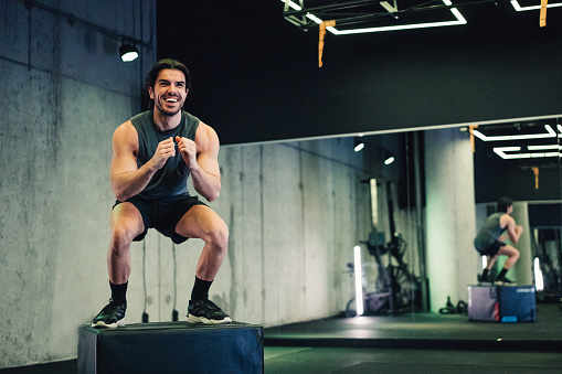 Shot of an athletic man jumping on a box while having sports training in a gym.