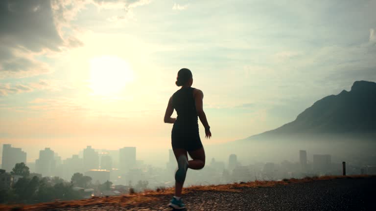 Back view sportswoman running  with dramatic sky and bright sunshine slow motion. Silhouette of female jogger during outdoor activity.