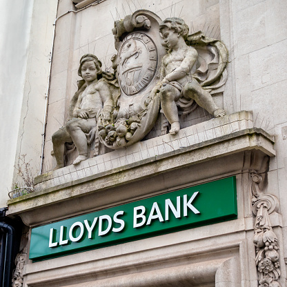 Statues of putti holding a cloth filled with of fruit and vegetables and bearing the date 1677 with a rearing horse logo outside a branch of Lloyds Bank in the High Street in Colchester, Essex, Eastern England. The stonework is protected by bird-repelling spikes. Lloyds’ black horse logo dates back to 1677 while Lloyds Bank itself dates back to 1765 - Lloyds inherited the logo from its acquisition of Barnetts, Hoares & Co in 1884.