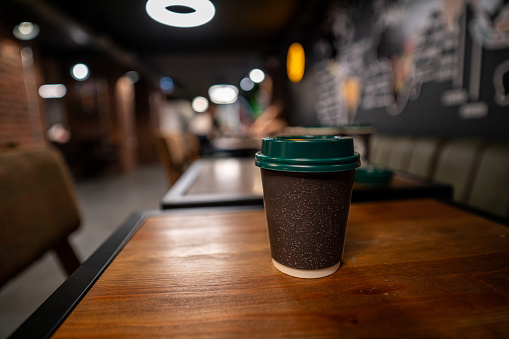 take a way coffee cup is on table focus on foreground cafe is background indoor close up horizontal still