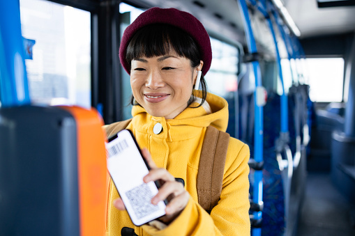 Female passenger using smart phone to validate ticket inside public bus transportation.