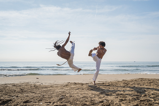 Men train capoeira on the beach - concept about people, lifestyle and sport. Training of two fighters