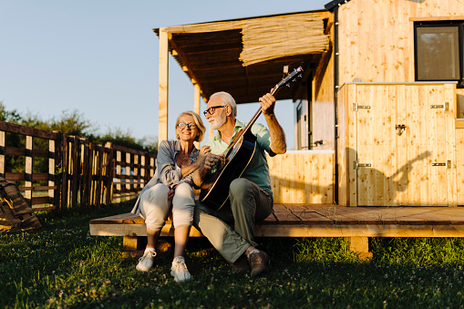 Senior couple playing acoustic guitar and enjoying on a patio of their glamping cabin