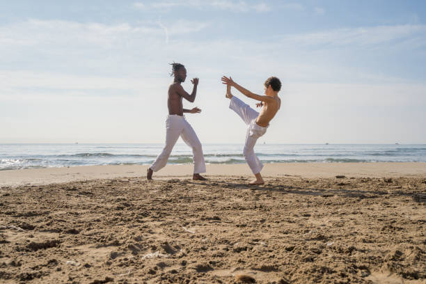 A boy takes capoeira lessons from his teacher on the beach.