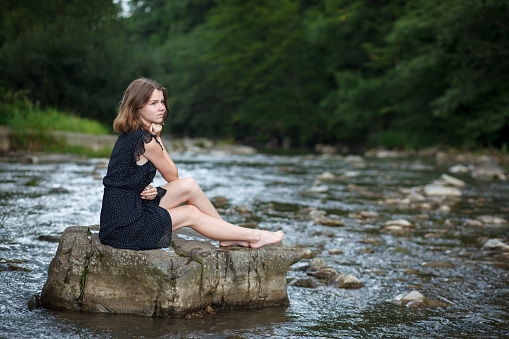 A girl sits on a stone in a mountain river.
