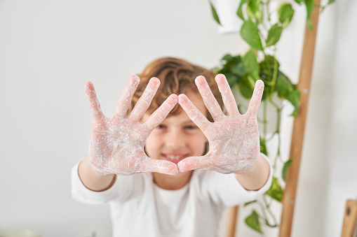 Selective focus of cheerful kid showing soapy hands in camera while having routine during morning hygiene routine