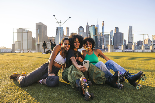 Three women friends shoot a selfie in front of New York skyline at sunset.